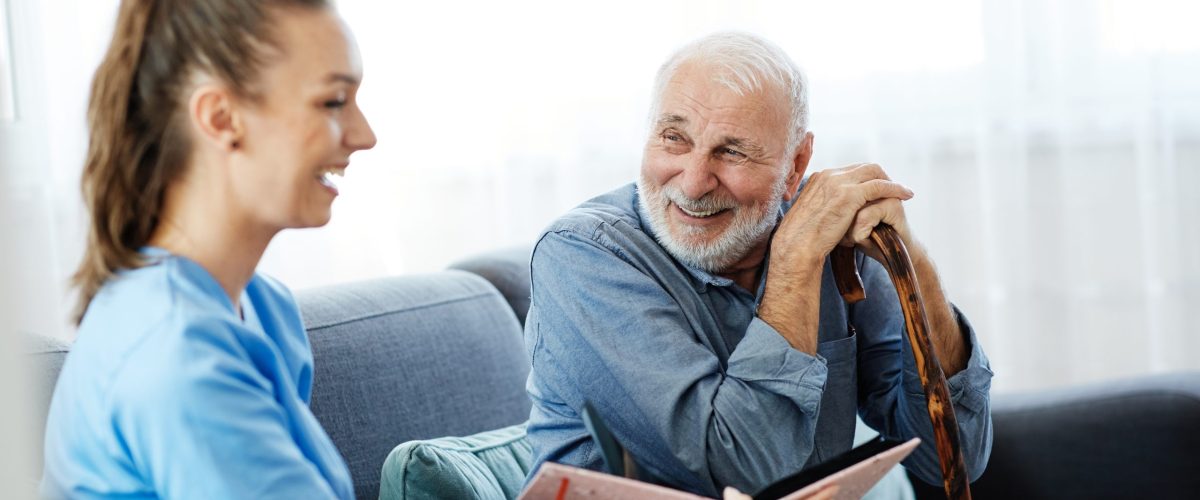 Doctor or nurse caregiver with senior man looking at photo album and picture  at home or nursing home